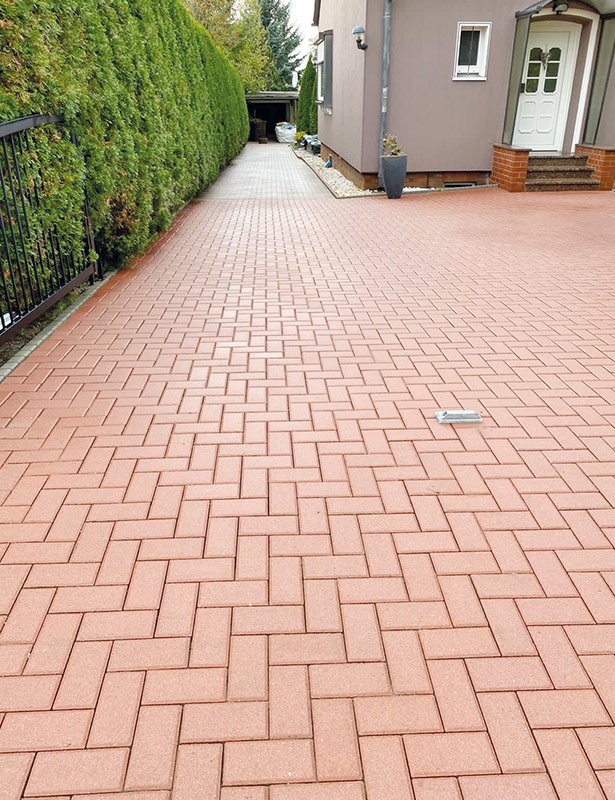 Gepflasterte Einfahrt neben Haus und Hecke
