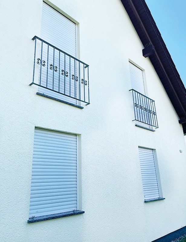 Hausfassade mit geschlossenen Jalousien und Balkongittern.